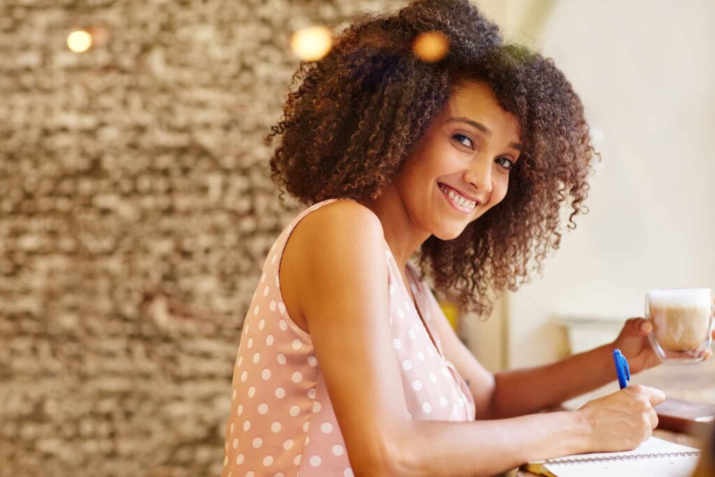 A young woman writing on a notepad while sitting in a coffee shop